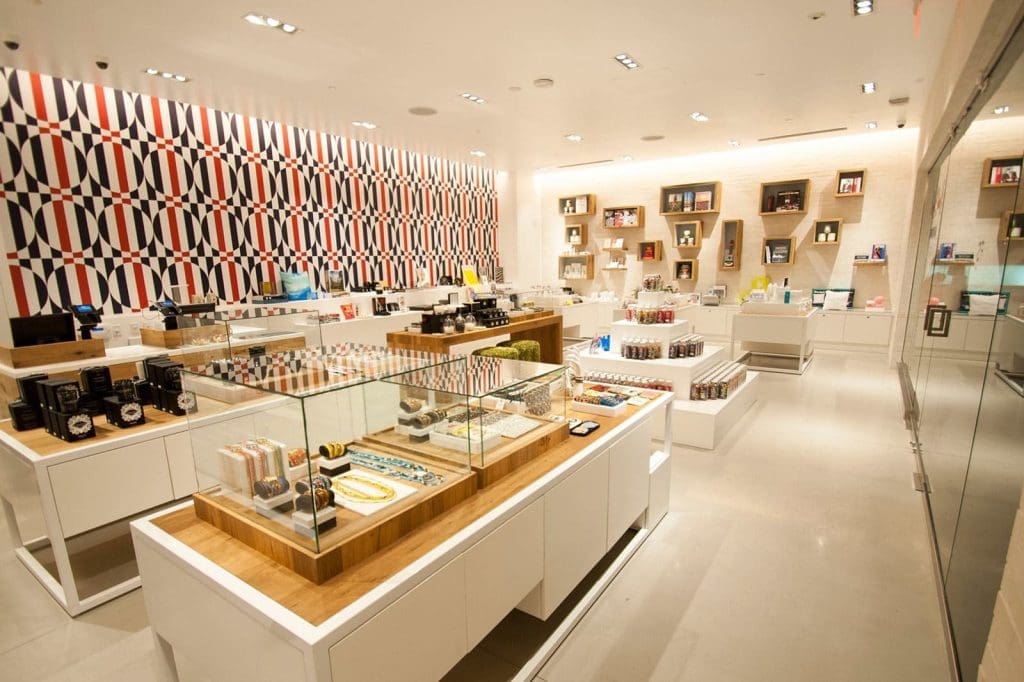 Modern retail store interior with well-lit displays of various products, glass cases, white shelves, and a geometric patterned accent wall.
