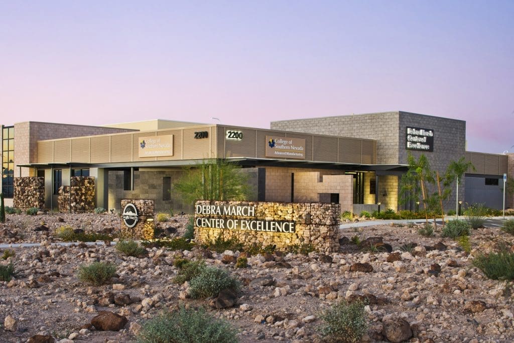 Modern medical facility, "Debra March Center of Excellence," with stone signage, desert landscaping, and clear building labels under a pastel sky.